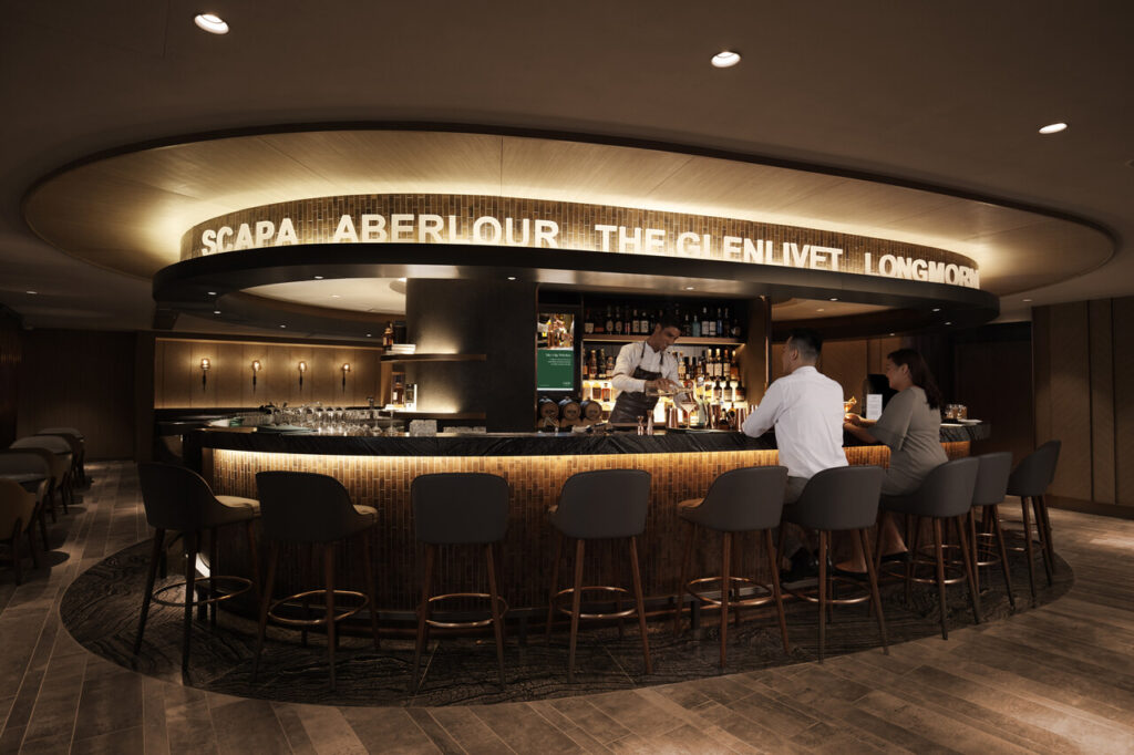 Using Beyond First by Plaza Premium Group, a sophisticated lounge bar with a circular design. The bar is elegantly lit, featuring a variety of spirits prominently displayed behind the bartender. The names "SCAPA," "ABERLOUR," "THE GLENLIVET," and "LONGMORN" are illuminated above the bar, highlighting the selection of whiskies available. Several patrons are seated on stylish bar stools, engaging with the bartender who is preparing drinks. The ambiance is warm and inviting, with modern decor and subdued lighting creating a relaxed atmosphere.