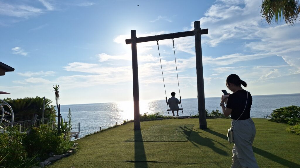 海邊草地上有鞦韆，背景是大海和藍天。